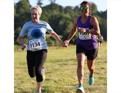 Two runners holding hands as they race across a grassy field on a sunny day.
