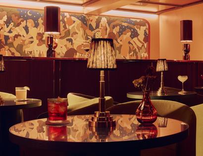 Elegant bar at Powdermills Hotel with round tables, cocktails, warm lighting, and a colourful mural backdrop.