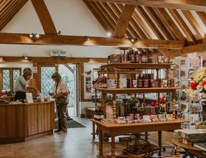 Gift shop at Pashley Manor Gardens with wooden beams, display tables of gifts, and two people at the counter.
