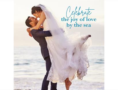 Bride and groom embracing on the beach, with text promoting celebrating love by the sea at Cooden Beach Hotel.