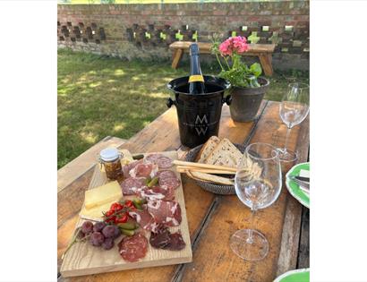 Outdoor table set with charcuterie, bread and glasses, alongside a chilled bottle of Mountfield wine in an ice bucket