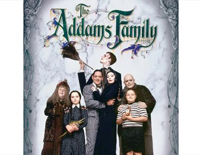 Promotional image for The Addams Family featuring the eccentric family posed beneath the title artwork.