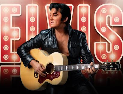 Performer as Elvis in black leather jacket playing guitar before illuminated “ELVIS” sign for Ben Portsmouth show.