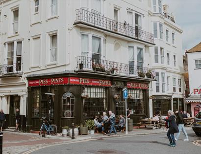 Exterior of The Albion pub on a Hastings street corner, with people sitting outside and nearby shops.