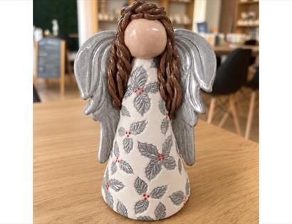 Handcrafted ceramic angel with silver wings and holly-patterned robe displayed during a Christmas pottery workshop
