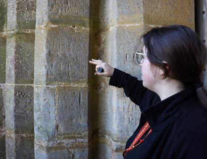Guide points out carved medieval graffiti on a stone pillar during a tour at Bodiam Castle.