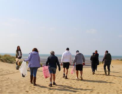 Community beach clean at the Gallivant, Camber, with volunteers walking across sand dunes carrying litter bags.