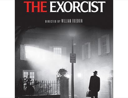Promotional poster for The Exorcist showing a figure beneath a streetlight outside a misty house at night.