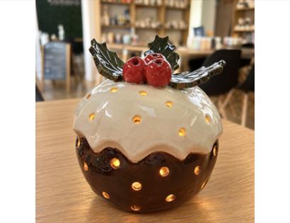 Handcrafted ceramic Christmas pudding lantern with holly decoration and glowing cut-out details from a pottery workshop