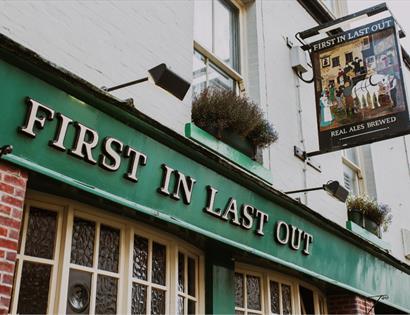 Exterior of the First In Last Out pub in Hastings with traditional signage and green frontage.