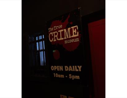Sign for the True Crime Museum entrance, venue for Bloody Bingo, illuminated against a dark interior backdrop.