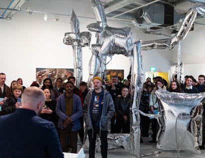 Crowd gathered around silver inflatable sculpture at Flatland Projects gallery opening in Bexhill.