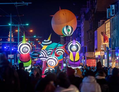 Crowds enjoy an 18 Hours event with large illuminated sculptures lighting up a city street at night.