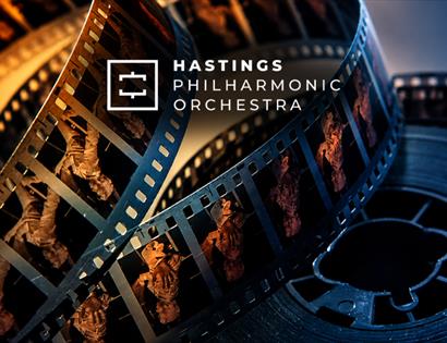 Film reels illuminated in blue and gold tones, promoting Hastings Philharmonic Orchestra's Beyond the Screen concert.