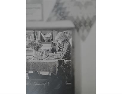 Black-and-white photograph of an artist working at a table in a studio, featured in the Annie Soudain Art Exhibition.