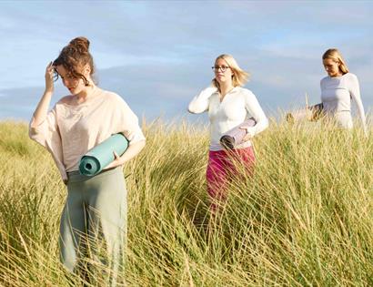 Participants carrying yoga mats walk through grassy dunes at The Gallivant for Strawberry Moonrise Yoga.