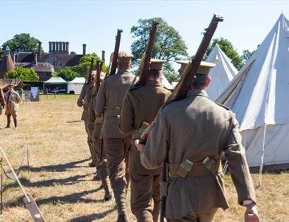 WW1 reenactors marching with rifles past canvas tents on a grassy field during a historical weekend at Bateman’s.