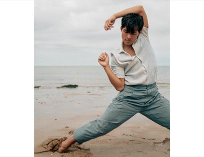 Yoga artist David Kam performs a fluid, expressive pose on a beach, arms raised and legs grounded in sand, from Beyond Asana.