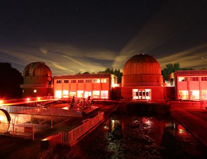 The Observatory Science Centre at night, illuminated in red with telescope domes under a starry sky.