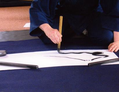 Person practicing Zen brushwork, painting a flowing black ink line on paper during a Summer Zen Brushwork workshop.