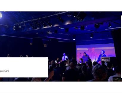 Live gig image for Oasiz at White Rock Theatre, showing a tribute band performing on stage to a packed audience under blue lights.