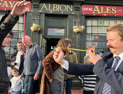 People compete in a traditional conkers match outside The Albion pub, watched by a crowd of spectators.