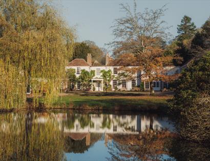 Crafted at Powdermills Hotel reflected in a lake, surrounded by autumn trees, showcasing serene countryside setting.