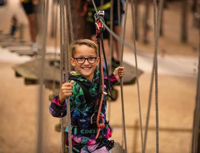Child navigating a rope bridge at Go Ape Bedgebury, holding onto ropes while in a safety harness.