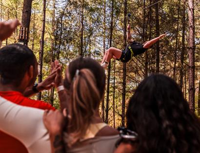 Adults-only group cheering as a participant rides a zip line through the forest at Go Ape treetop adventure.