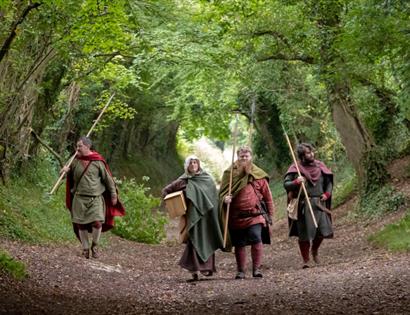 Historical reenactors walking along a woodland path with spears and cloaks, promoting Meet the Haestingas at Hastings Museum & Art Gallery
