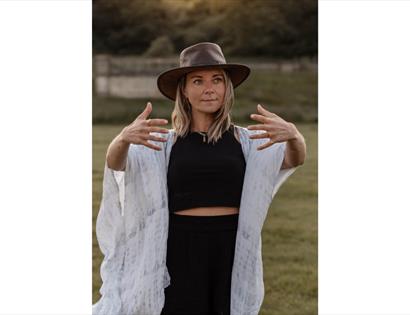 Facilitator stands outdoors with arms open in a guided movement pose, promoting Summer Transformational Breathwork at The Gallivant.