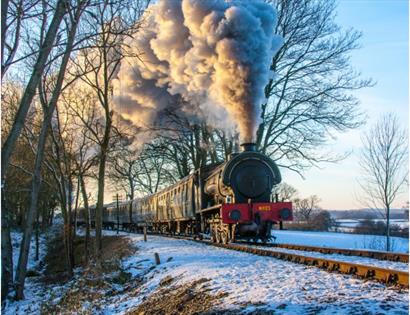 Steam locomotive travelling through a snowy countryside, billowing steam, during the Steam Into New Year railway event.