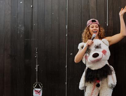 Performer in a bear-themed costume holding a microphone onstage during ‘New Work Night – Titus Andronicus.’