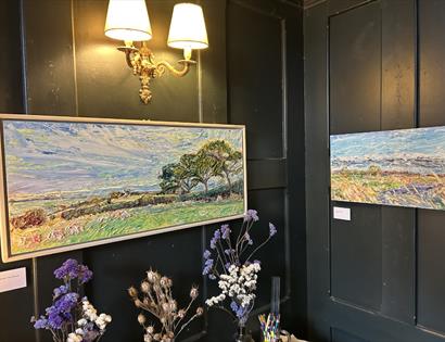 Landscape paintings by Wendy Cox displayed at The Crown in Hastings, with textured scenes of countryside and sky.