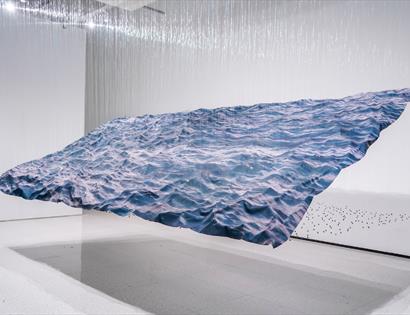 Large suspended wave-like installation with ocean imagery and hanging threads, Miguel Rothschild exhibition at Hastings Contemporary.