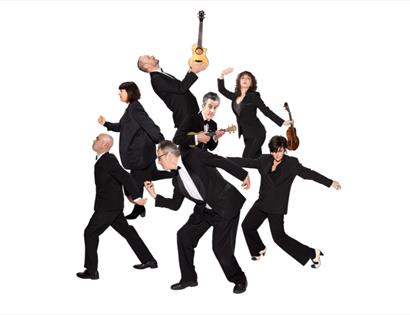 The Ukulele Orchestra of Great Britain in black suits, posed dynamically with ukuleles against a plain white background.