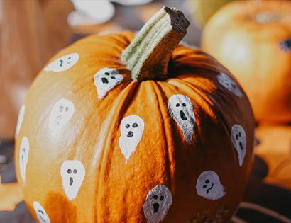 Close-up of a pumpkin decorated with painted ghost faces, promoting an autumn storytelling and woodland event