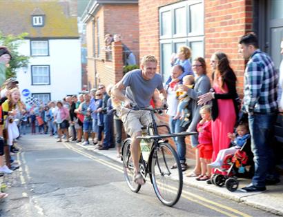 Hastings Old Town Carnival Week bicycle race draws crowds along a narrow street lined with spectators.
