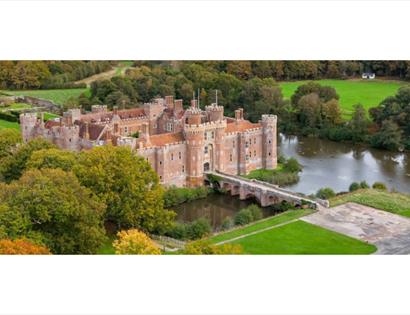 Aerial view of Herstmonceux Castle surrounded by autumn trees and lawns.