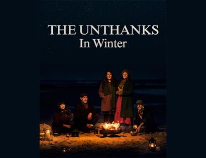 Promotional image for The Unthanks’ album "In Winter", showing five musicians around a beach fire at night.