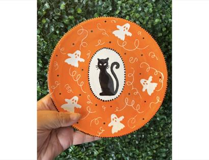 Hand-painted Halloween plate featuring a black cat, friendly ghosts and orange seasonal design at a pottery workshop.