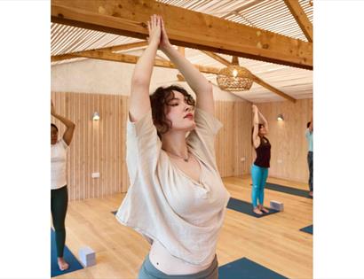 Group of people in a bright studio practicing a raised‑arm yoga pose on mats.