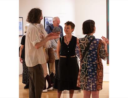 Visitors in conversation during a gallery event at De La Warr Pavilion, surrounded by exhibition artworks.