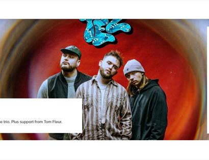 Promotional image of indie trio TEZ standing before a colourful abstract backdrop, with event details and White Rock Hastings branding.