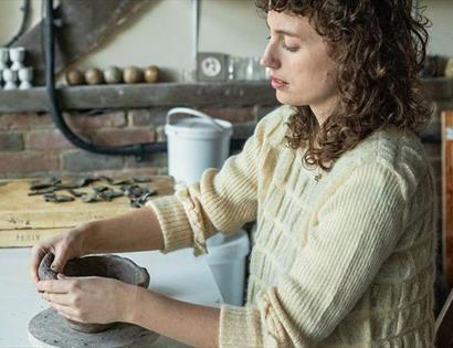 Person shaping a clay vessel during a pottery workshop at Crafted at Powdermills, inspired by haunted houses.