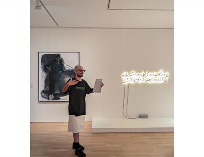 Person leading a gallery tour beside contemporary artworks and a neon installation at De La Warr Pavilion.