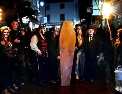 Torchlit Hastings Voodoo Fest parade with costumed participants, painted faces and a coffin carried through night streets.
