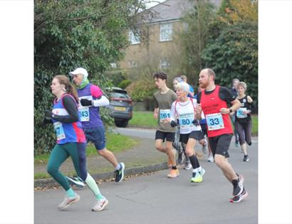 Promotional image for Crowborough 10k & 5k, showing participants running on a road through a residential area.
