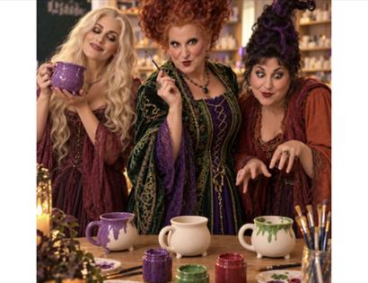 Three Hocus Pocus-inspired characters painting pottery mugs at a themed food and pottery painting event.
