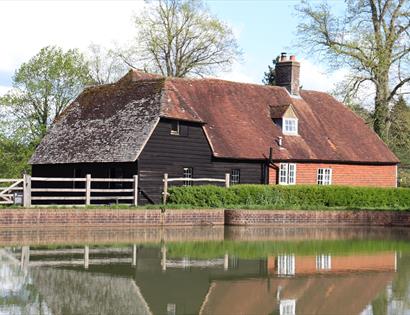 Park Mill at Bateman’s during Mill Weekend, with a historic red‑tiled mill building reflected in the surrounding water.